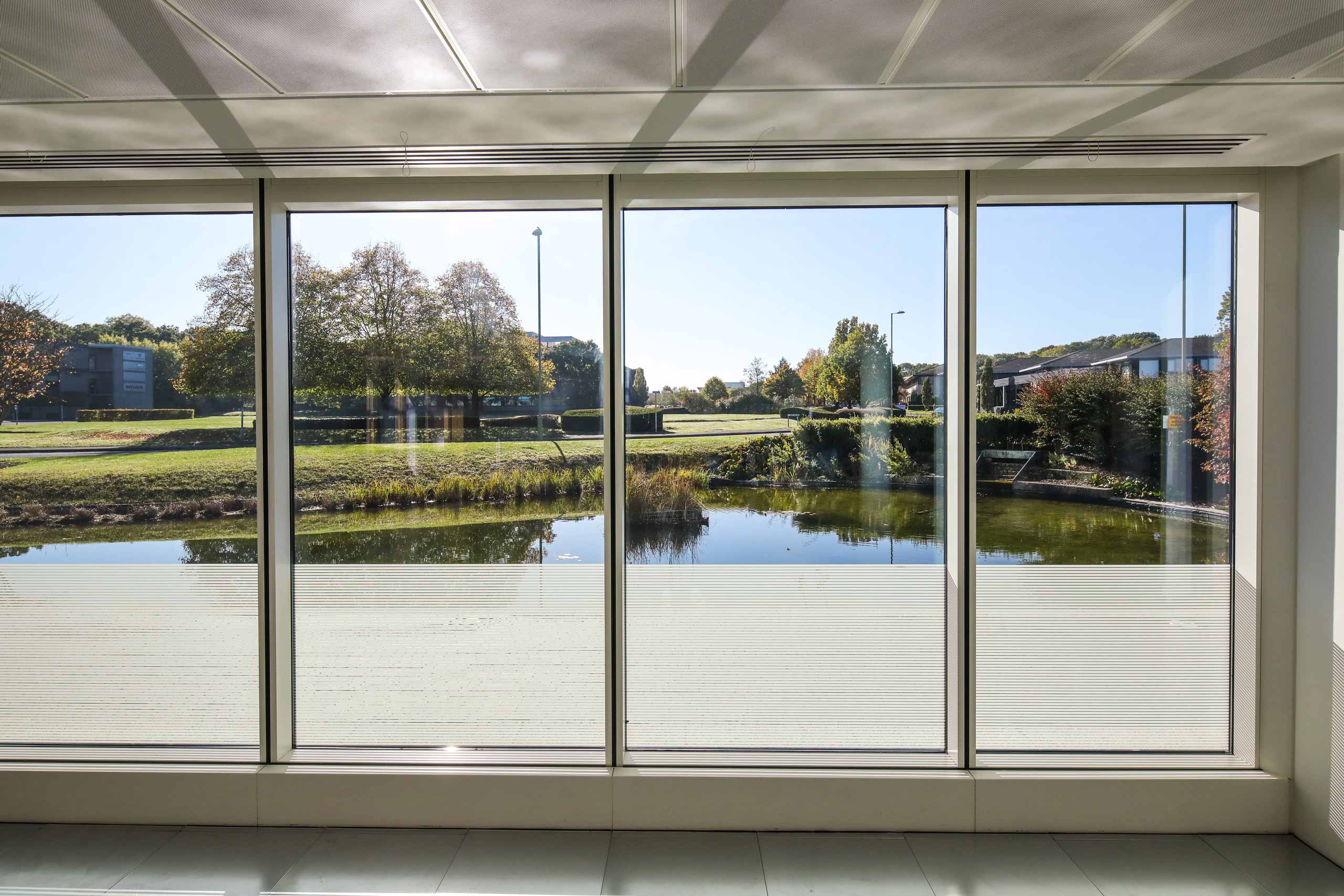 An office with large windows overlooking a pond.