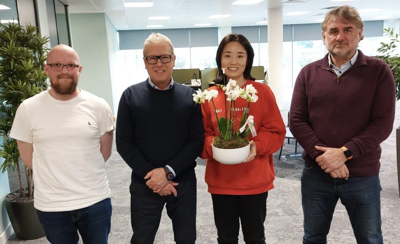 Four people standing next to a potted plant in an office.