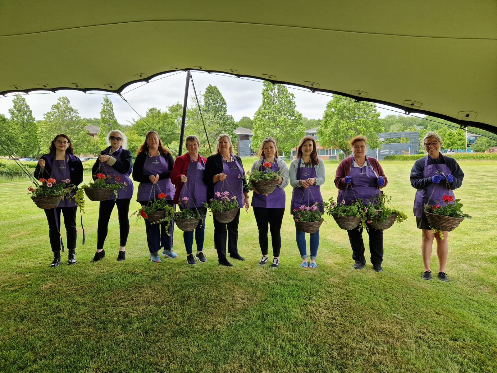 A group of women in purple aprons standing under a tent.