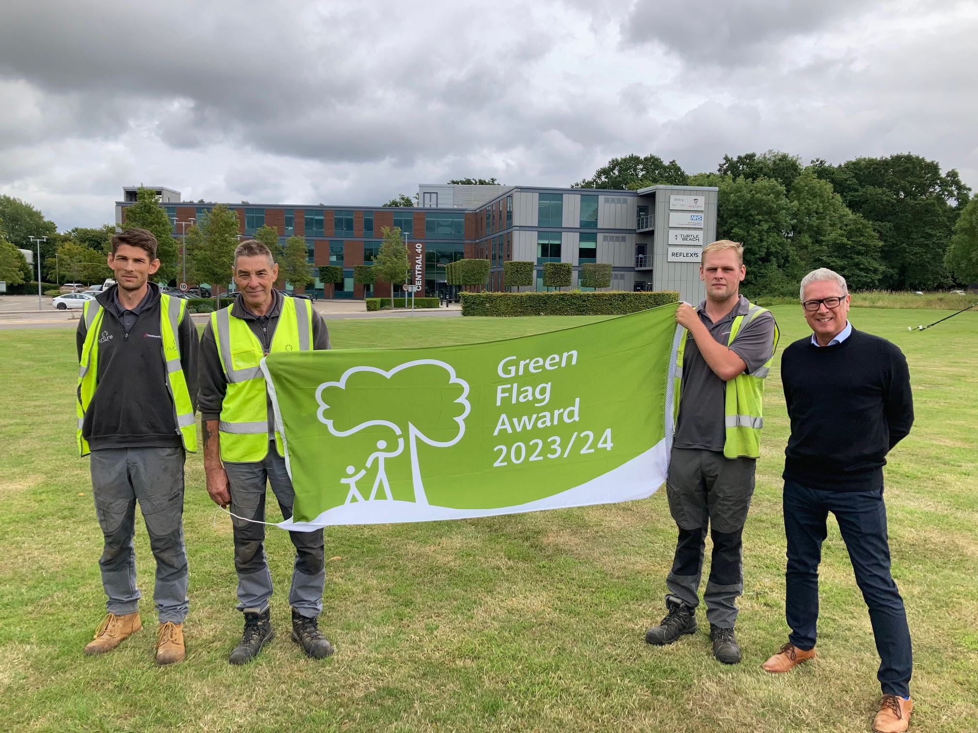 Four men standing with a green flag in front of a building.