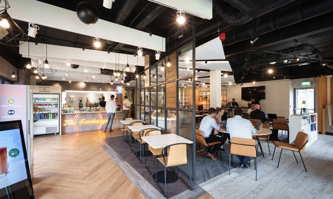 The interior of a collaborative space coffee shop with people sitting at tables.