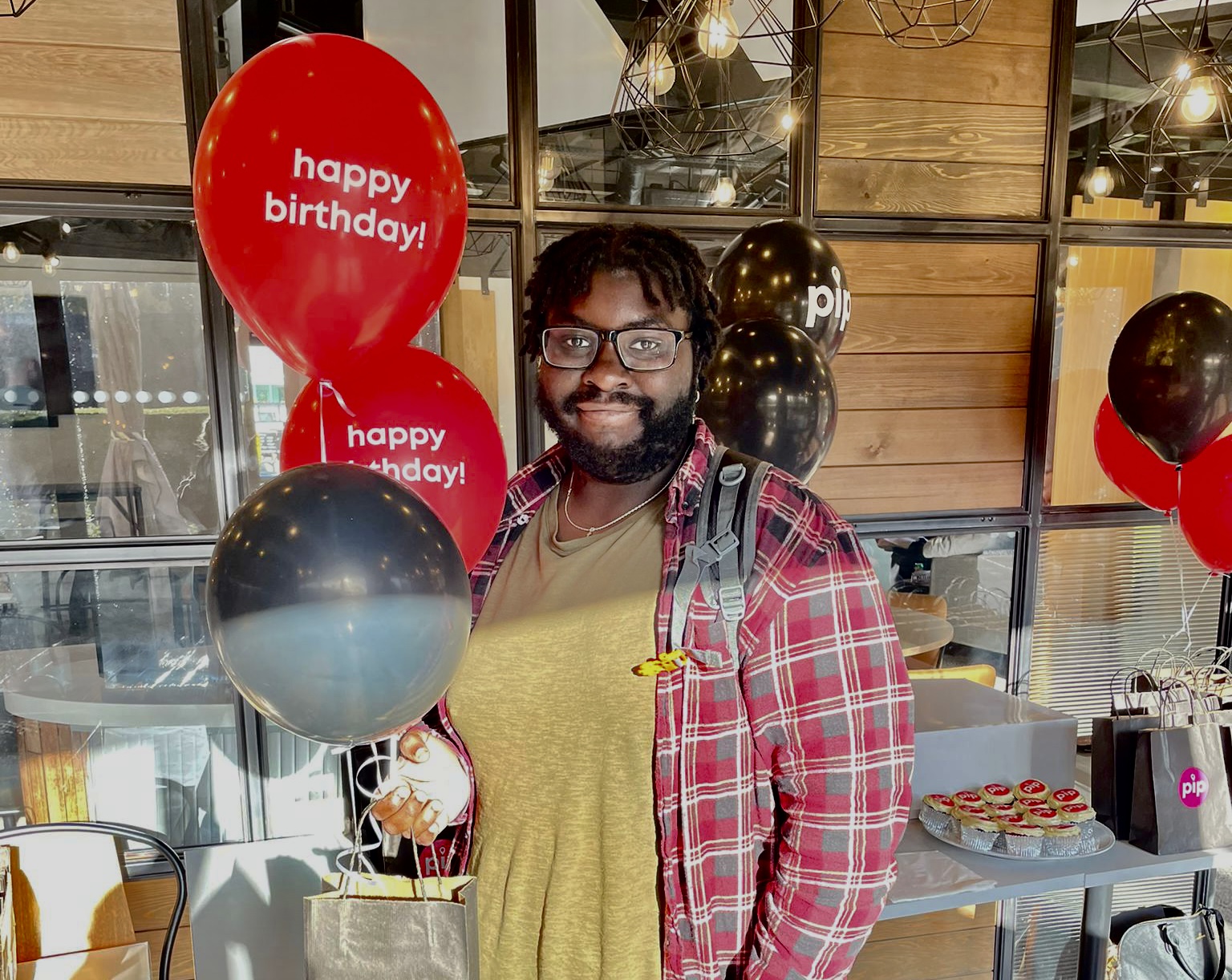A man standing in front of a birthday cake and balloons.