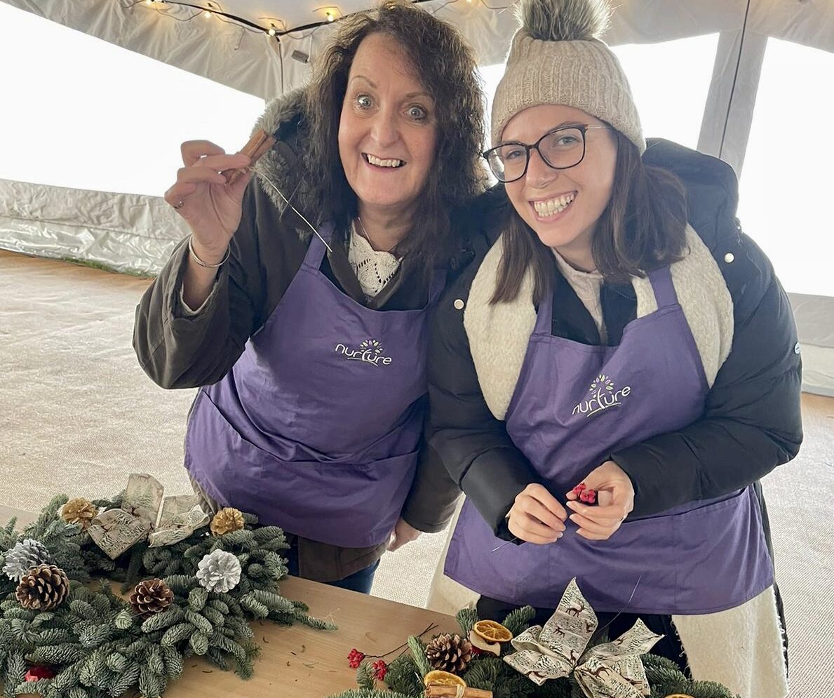 Two women posing in front of a table with wreaths.